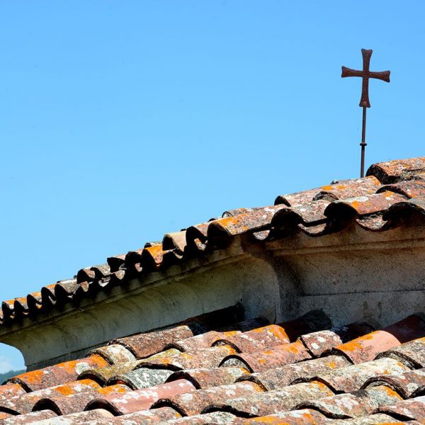 Olot.- Capella de Sant Martirià. Situada a la rotonda de Santa Pau. Entre teulades sobresurt l'unic element decoratiu; una alta creu de ferro (6/2017)