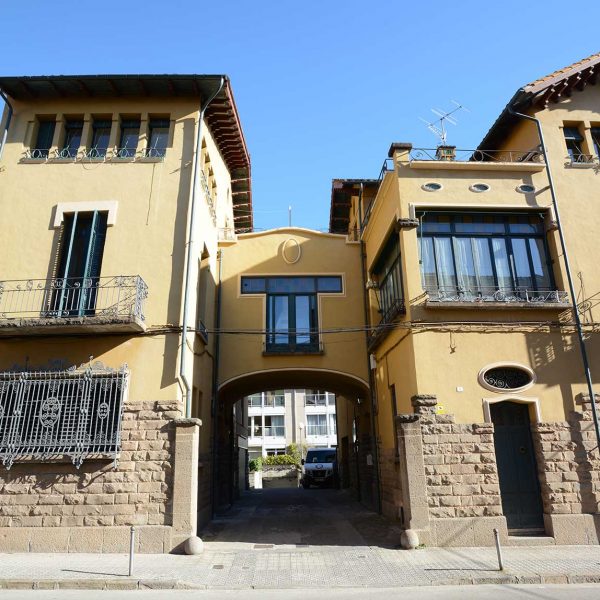 Olot.- Fàbrica Descals, d'estil noucentista de J. Roca i Pinet, S. XX. Vista frontal de la façana amb una tribuna cobrint el pas cap l'interior (2/2017)