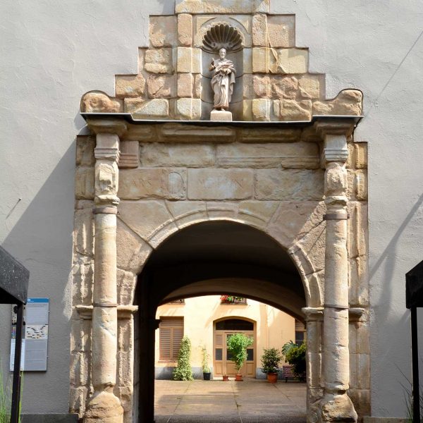 Olot.- Porta renaixentista de la façana de l'antic hospital de Sant Jaume d'arc de mig punt flanquejat per columnes i al damunt té l'imatge del Sant (6/2017)