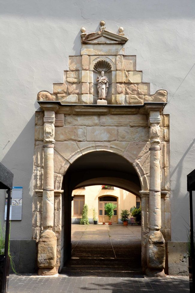 Olot.- Porta renaixentista de la façana de l'antic hospital de Sant Jaume d'arc de mig punt flanquejat per columnes i al damunt té l'imatge del Sant (6/2017)