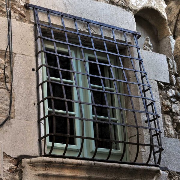 Girona.- Casa Colls/Labayen, S. XII/XIV/XX d'estils romànic i gòtic articulada al voltant d'un pati. Finestra enreixada de tires llises (3/2014)