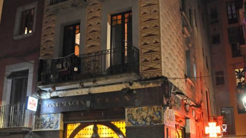 Girona.- Farmàcia Plana, situada a l a planta baixa d'un edifici noucentista. Te dues grans portes als angles i un fris de plafons ceràmics (11/2013)