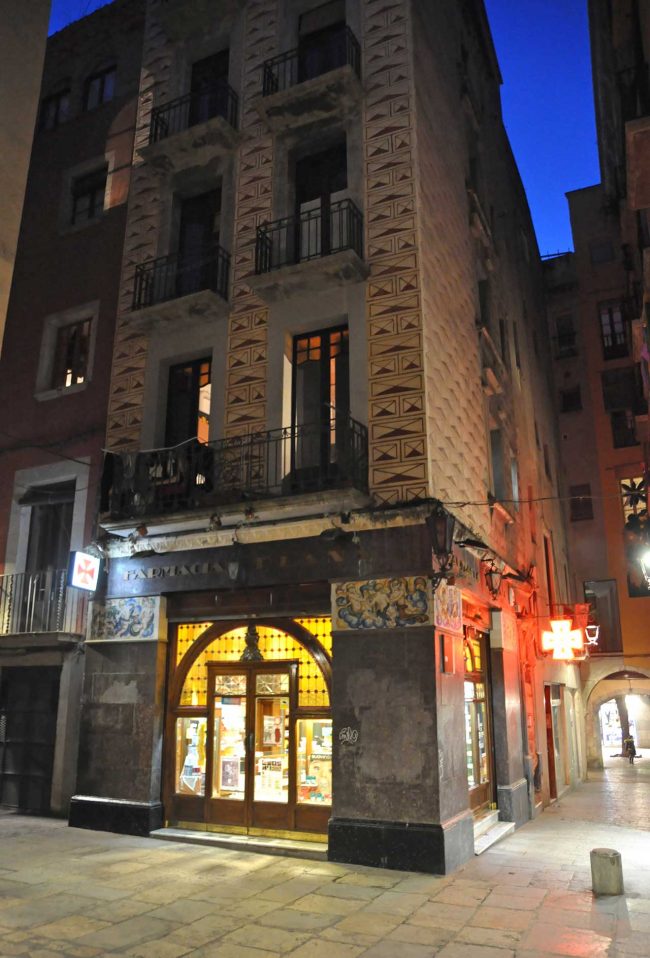 Girona.- Farmàcia Plana, situada a l a planta baixa d'un edifici noucentista. Te dues grans portes als angles i un fris de plafons ceràmics (11/2013)