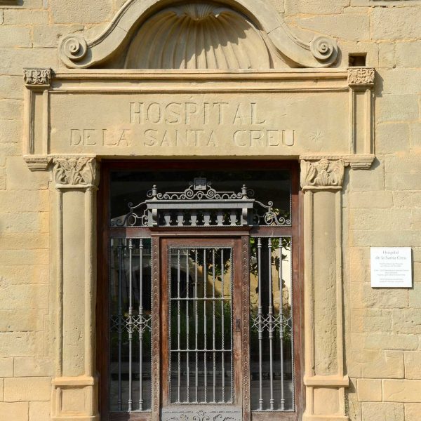 Vic.- Hospital de la Santa Creu, S. XIV. Porta renaixentista amb columnes motllurades i capitells i una petxina sobre la llinda (7/2018)