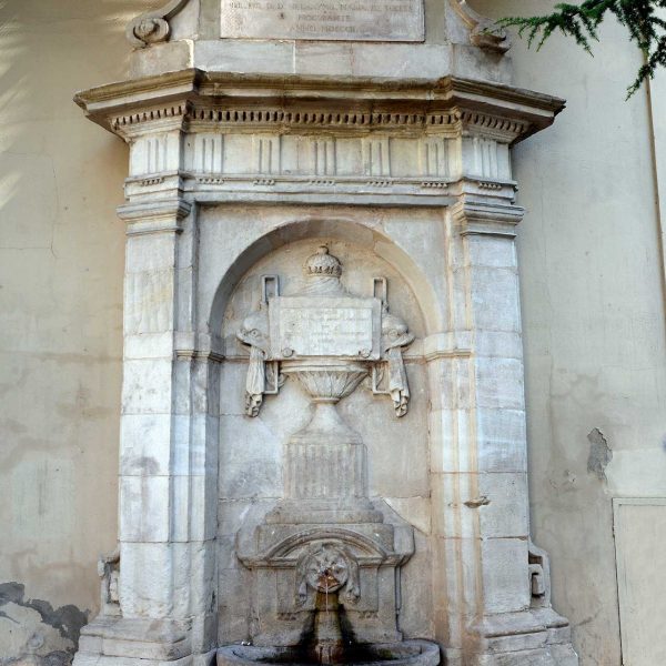 Lleida.- Font de l'Hospital, neoclàssica/monumentalista del S. XX flanquejada per pilastres que suporten un fris. A l'interior hi ha un relleu en forma de copa (9/2018)