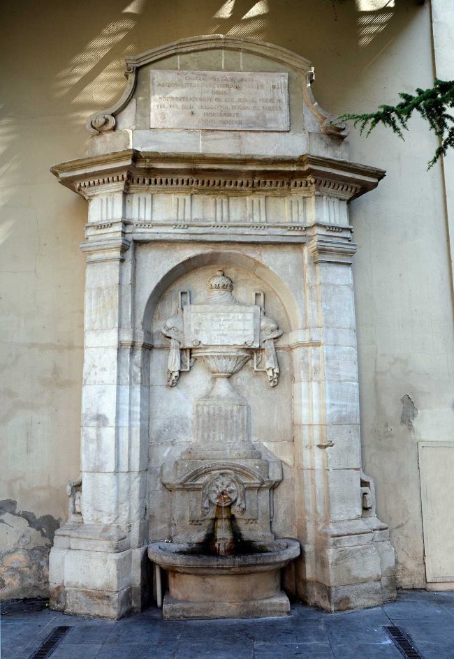 Lleida.- Font de l'Hospital, neoclàssica/monumentalista del S. XX flanquejada per pilastres que suporten un fris. A l'interior hi ha un relleu en forma de copa (9/2018)