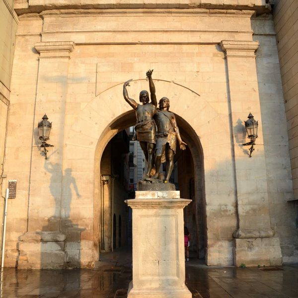 Lleida.- Portal de l'arc del Pont, neoclàssic del S. XVIII d’arc de mig punt coronat per un frontó triangular que emmarca el monument d'Indíbil i Mandoni (9/2018)
