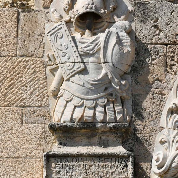 Tarragona.- Portal barroc de Sant Antoni construït l’any 1737. Relleus de trofeus militars romans sobre una base commemorativa de la construcció del portal (30/2021)