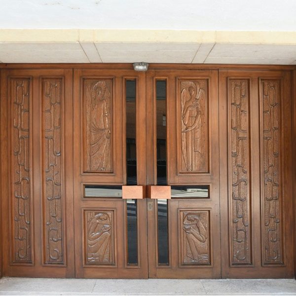 Tortosa.- Església Mare de Déu dels Dolors inaugurada l’any 1970 – Porta rectangular amb batents de fusta decorada amb quatre baix relleus centrals (7/2022)