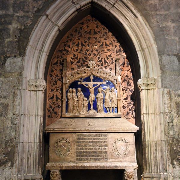 Barcelona.- Capella de Santa Llúcia - Sarcòfag del mur de l’esquerra del canonge Francesc de Santa Coloma del S. XIV i al damunt un calvari de pedra sobre un fons vidriat blau (3/2026)