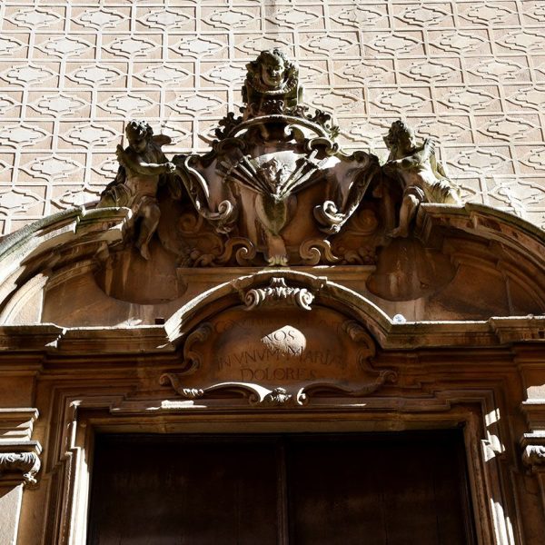 Vic.- Església barroca dels Dolors, S. XVIII de Josep Morató – Façana amb un gran frontó trencat amb dos querubins assentats sostenint l’emblema del Sagrat Cor (2/2020)