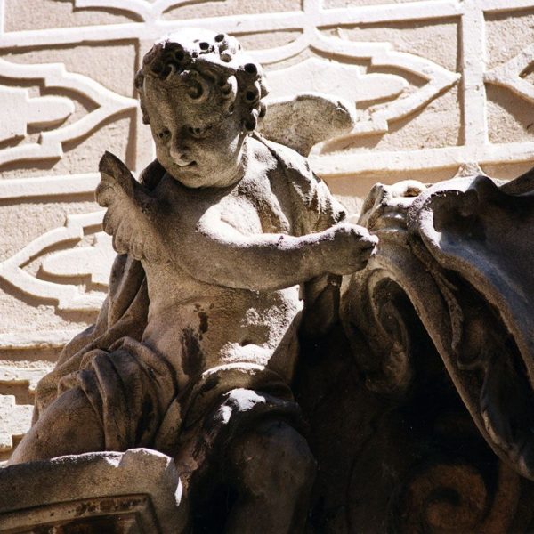 Vic.- Església barroca dels Dolors, S. XVIII de Josep Morató – Un dels querubins assentat en el frontó de la portalada sostenint l’emblema del Sagrat Cor (8/2000)